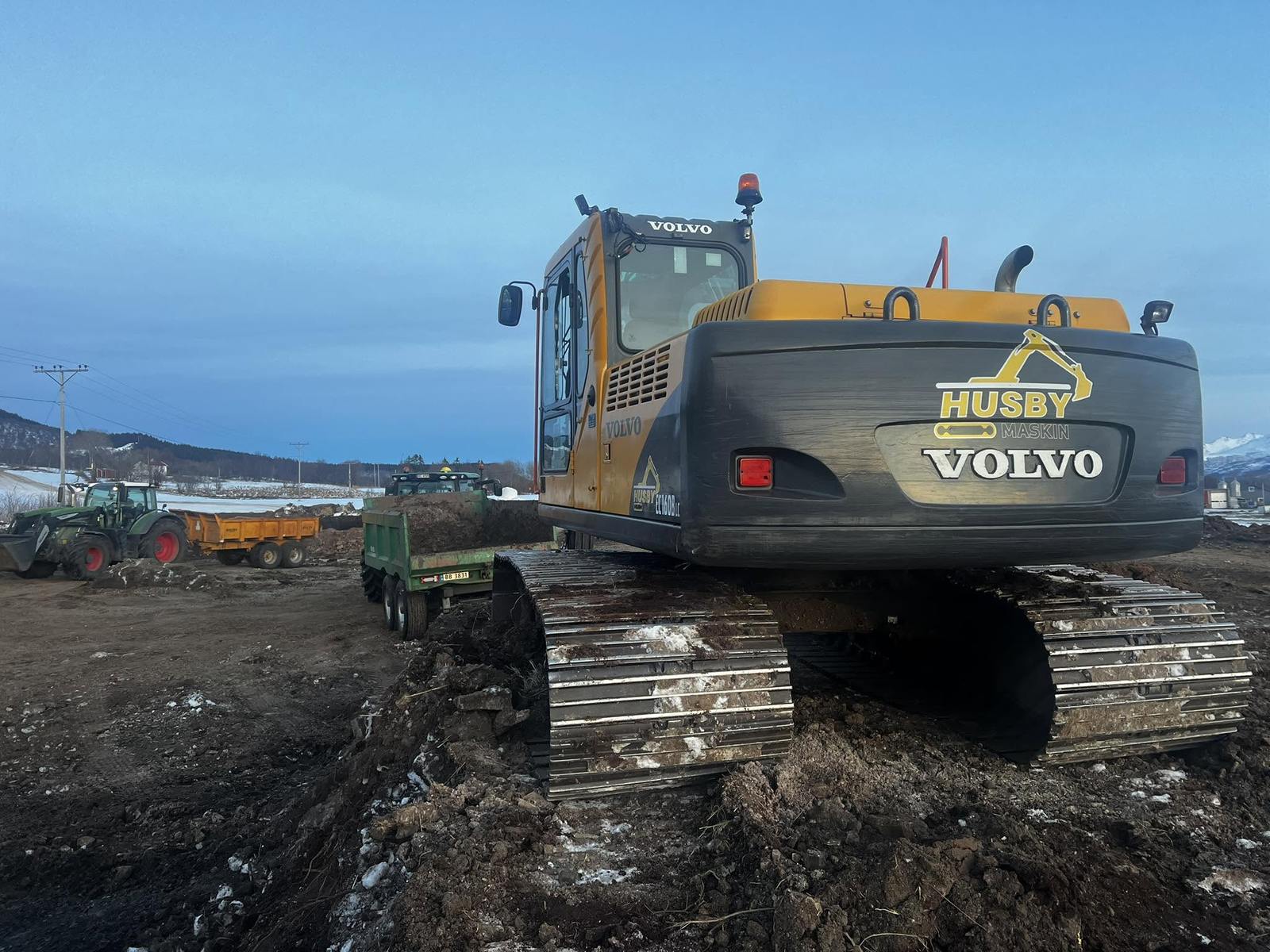 Volvo gravemaskin fra Husby Maskin med Fendt-traktor og henger på anleggsområde i Vesterålen en vinterdag